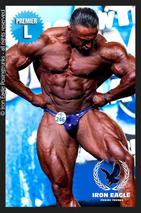 Bodybuilder wearing blue Delphinium Mystique posing trunks onstage, flexing in a competition pose. - Delphinium Mystique - Premier / S / With
